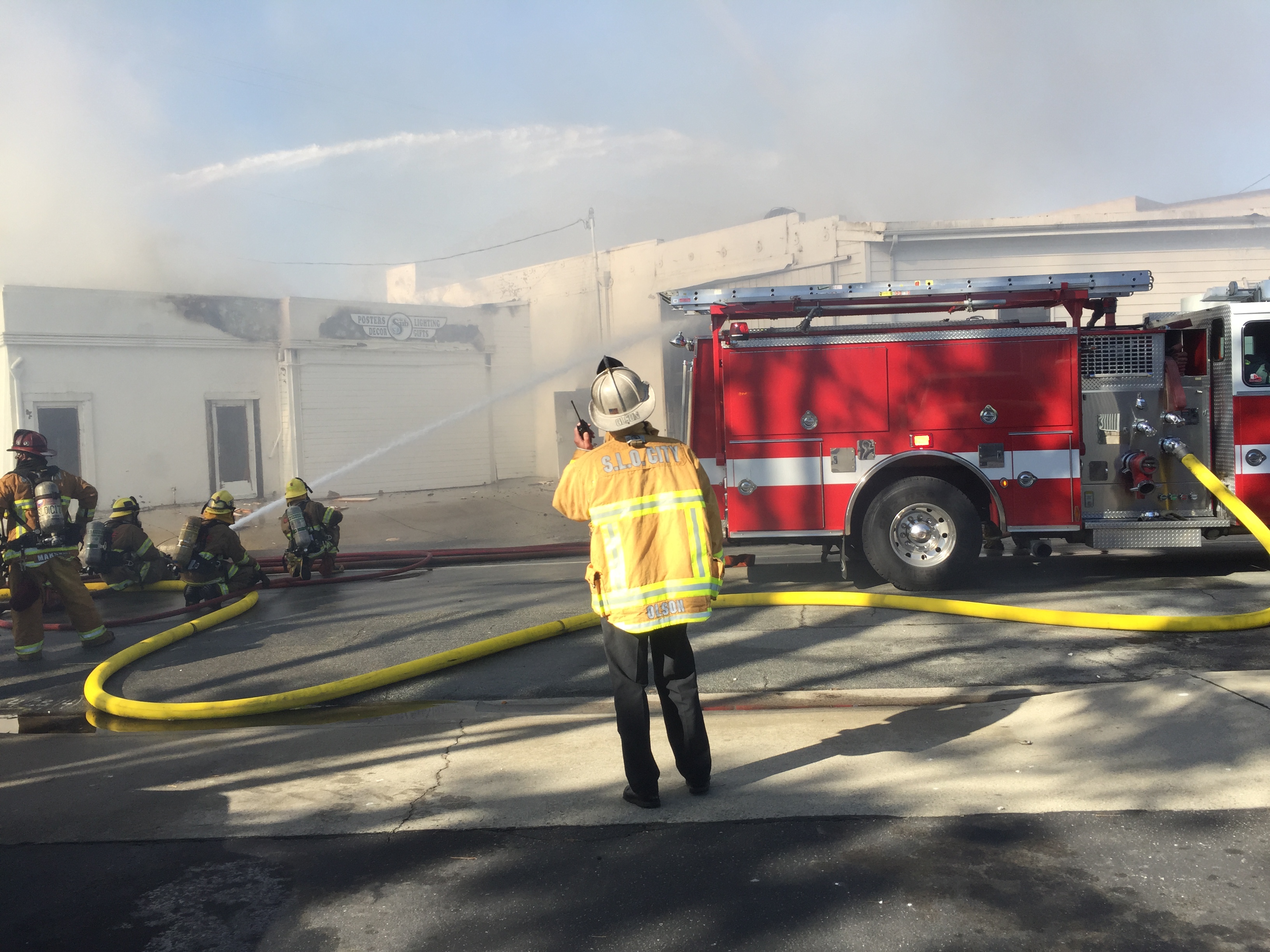 SLOCF Chief Garret Olson watches firefighters sit outside burning building spraying water.